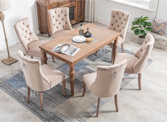 Eetkamer met zes beige fluwelen stoelen rond een houten tafel. Stoelen hebben knopquilting en metalen ringen op de rug.