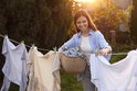 Een lachende vrouw hangt kleding op een waslijn op een zonnige dag.