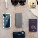 Grijze Xtorm powerbank op een achtergrond, omringd door een telefoonhoesje, zonnebril, lippenstift en paspoort.