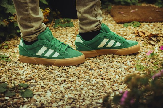 Groene Adidas sneakers met witte strepen en bruine zolen, gedragen door iemand met een beige broek.