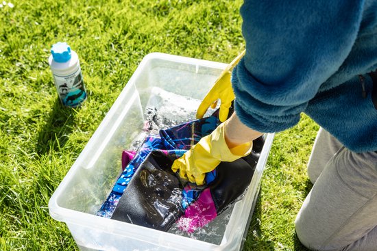 Wetsuit wassen in een bak met water, met gele handschoenen