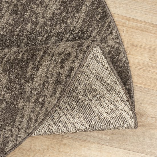 Detail van de achterkant van een rond bruin vloerkleed met textielpatroon.