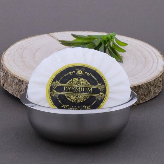 Ronde scheerzeep met gele en zwarte verpakking, 'Premium Shaving' erop, in een metalen kom.