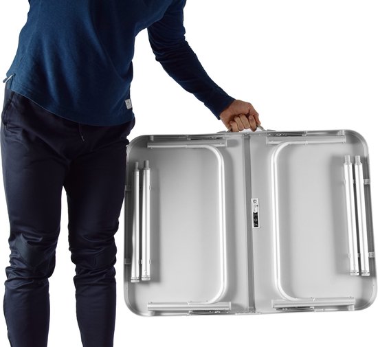 Man met blauwe trui draagt ingeklapte zilverkleurige campingtafel bij handvat.