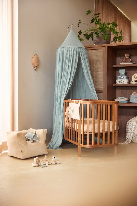 Babykamer met houten ledikant, hemel, fauteuil en speelgoedtrein.