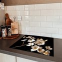 Glazen snijplank met witte en gouden bloemen, op een keukenblad.