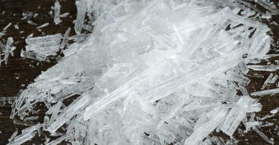 Close-up van heldere, naaldvormige menthol kristallen op een donkerhouten achtergrond.
