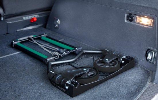 Een opgevouwen, zwarte steekwagen met groene details en wielen, in de kofferbak van een auto.