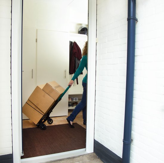 Een vrouw rijdt met een steekwagen met drie grote dozen naar binnen, door een deuropening.