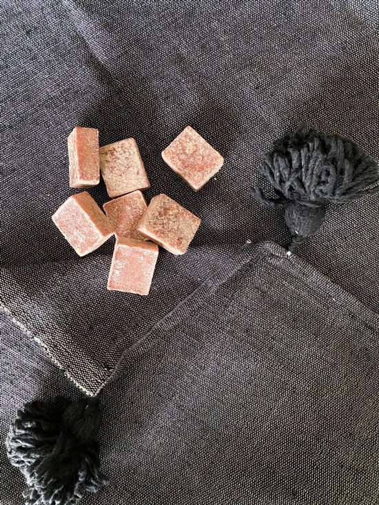 Zeven roze amberblokjes met een lichte korrel op een donkere achtergrond, naast een zwart pompon.
