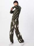 Model in olijfgroene trui met zwarte V-strepen, met beanie en broek met patroon.