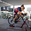 Vrouwen in USA-tenues trainen op racefietsen op rode Fietstrainers op een balkon met uitzicht op de stad.