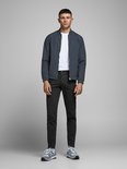 Man in zwarte chino broek, donkergrijs jack, witte sneakers.