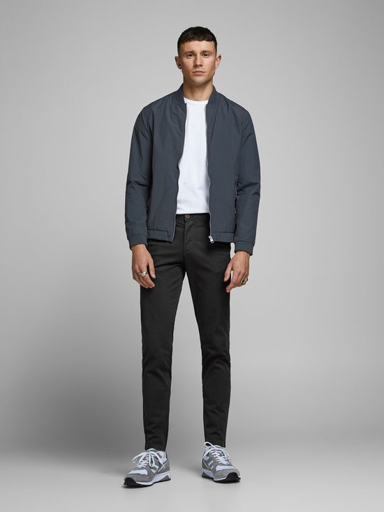 Man in zwarte chino broek, donkergrijs jack, witte sneakers.