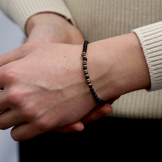 Model draagt een zwarte agaat en hematite kralen armband met gouden accenten.