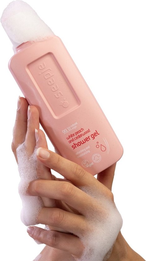 Handen met schuim houden een roze Seepje fles douchegel met witte perzik en cederhout vast.