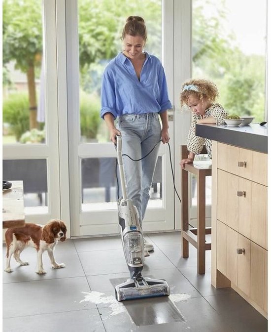 Vrouw in blauw shirt en spijkerbroek maakt de vloer schoon met een Bissell Crosswave C3 Select steelstofzuiger.