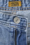 Detail van lichtblauwe jeans: tailleband met gele label 'JACK & JONES', knoop en rits.