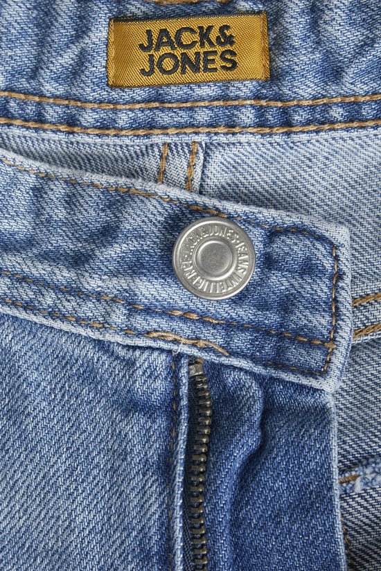 Detail van lichtblauwe jeans: tailleband met gele label 'JACK & JONES', knoop en rits.