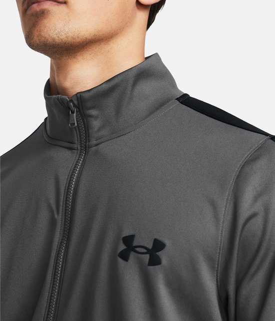 Close-up van de kraag en rits van een grijs Under Armour trainingsjack met zwart logo op de borst.