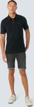 Model draagt een zwart poloshirt en een grijze spijkerbroekshort.