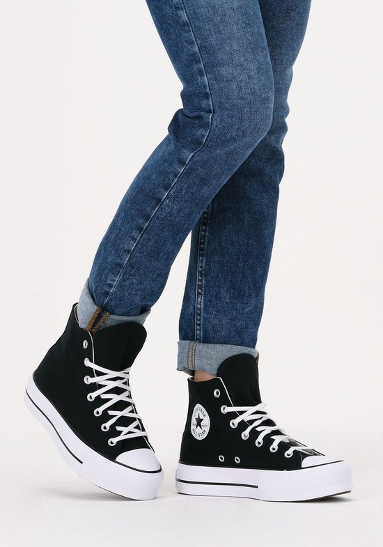 Model in een zwarte Converse Chuck Taylor All Star Lift sneakers met witte veters en een dikke witte zool, gecombineerd met een spijkerbroek.