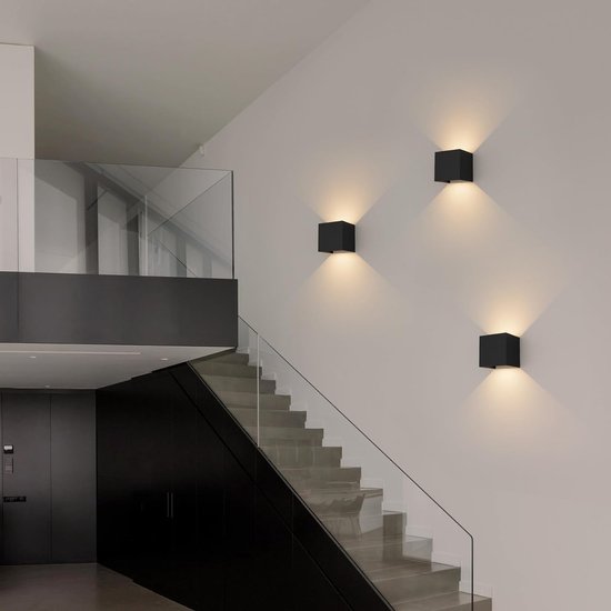 Moderne hal met een trap, verlicht door drie zwarte kubuswandlampen.