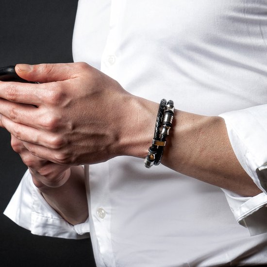Gevlochten zwarte armband met zilverkleurige details, gedragen door een man in wit overhemd, houdt telefoon vast.