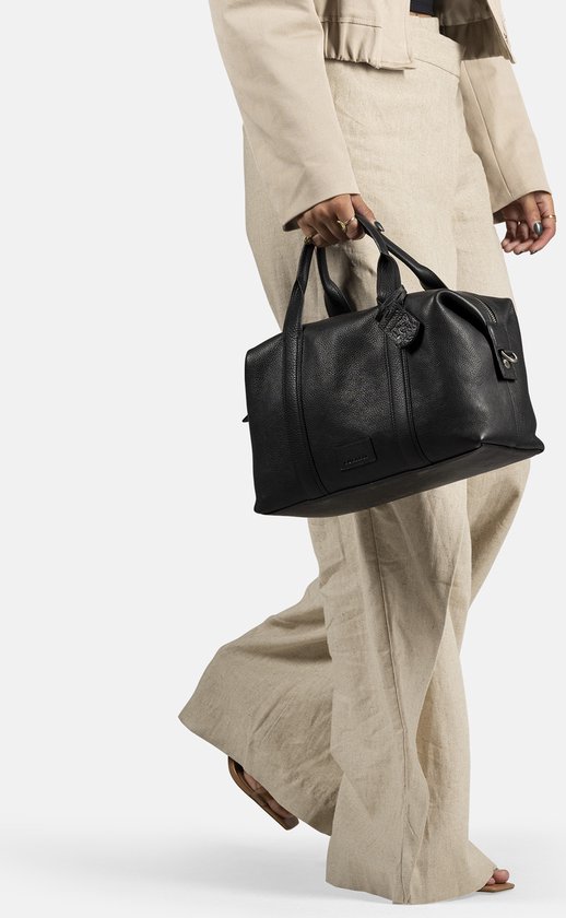 Vrouw met beige outfit draagt een zwarte leren Burkely bowler tas met hangend label.