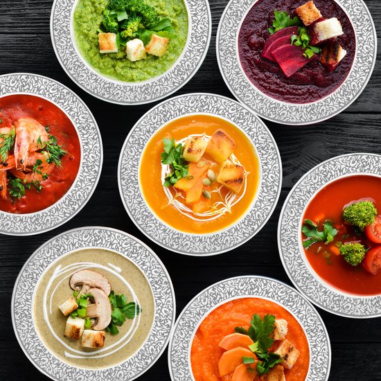 Zeven verschillende soepen in witte kommen met zilveren rand: groente, biet, garnalen, pompoen, courgette, champignon en wortel.