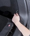 Hand haakt zwarte bumperbeschermer aan bevestigingspunt in zilveren stationwagen.