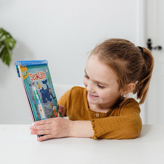 Une fille avec des couettes regarde un livre de coloriage magique à l'eau 'Sea Life'.