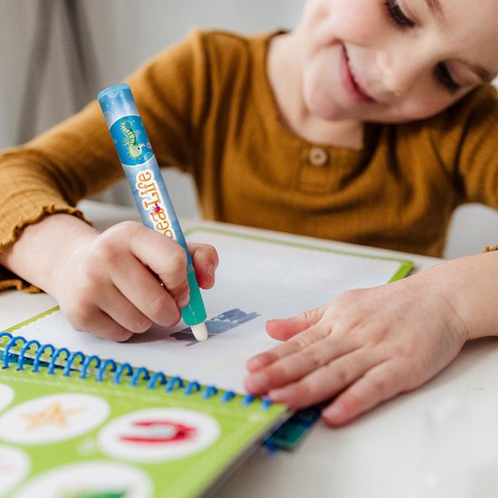 Gros plan d'une fille coloriant avec un stylo à eau bleu avec un hippocampe dans un livre Aqua Magic.