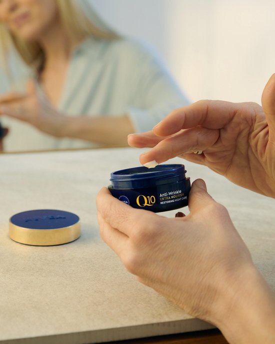 Een vrouw neemt met haar vingers crème uit een Nivea Q10 potje, met deksel ernaast.