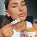 Gouden gelmasker en spatel in de hand van een vrouw. "VITAMIN C GLOW GEL MASK".
