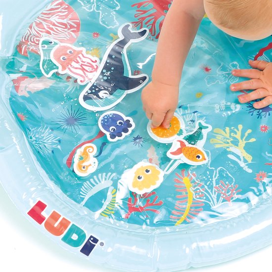 Baby's handje raakt een vrolijk visje aan op een lichtblauwe water speelmat met zeedieren.