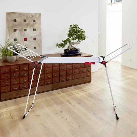 Étendage Vileda Infinity Flex plié, debout contre une armoire en bois dans une chambre.
