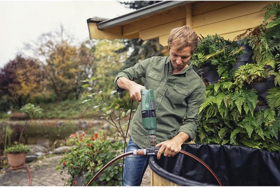 Man met boormachine bevestigt GARDENA voorzetpomp aan tuinslang bij een vijver.