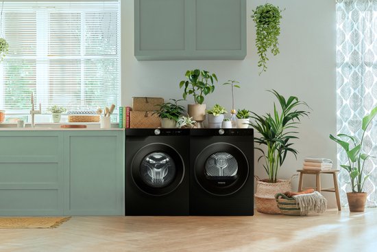 Twee zwarte Samsung wasapparaten, wasmachine en droger, in een lichte, moderne keuken met veel planten.