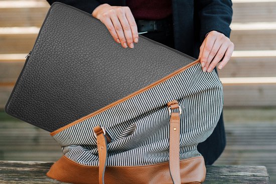 Une femme met une housse d'ordinateur portable noire texturée dans un sac à rayures.