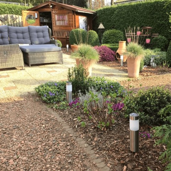 Zilverkleurige solar paaltjes met witte verlichting, geplaatst in een tuin met grindpaden en planten.