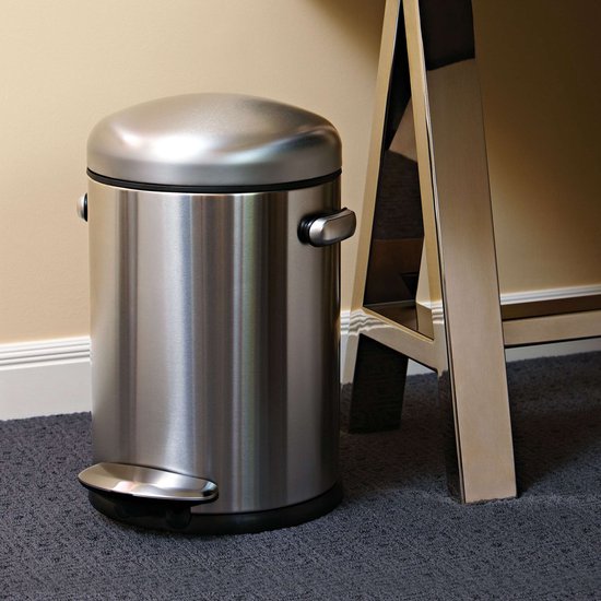 RVS pedaalemmer met ronde deksel, staand op grijs tapijt naast een glimmende metalen tafelpoot.