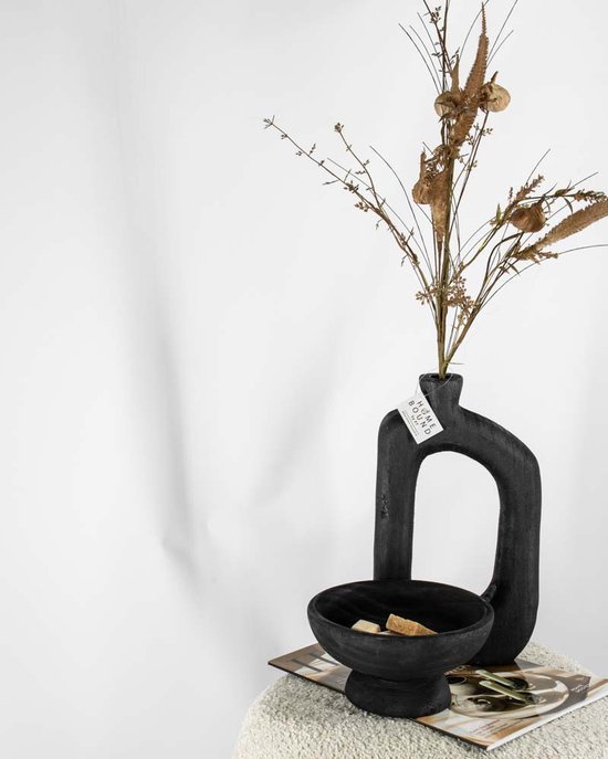 Zwarte houten vaas met ovale opening, gevuld met droogbloemen, met label. Naast een kommetje.