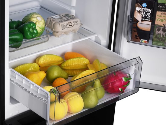 Open crisperlade van een zwarte koelkast gevuld met exotisch fruit, peren en appels.