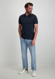 Man met donkerblauw poloshirt en lichtblauwe jeans, met opgerolde pijpen en witte sneakers.