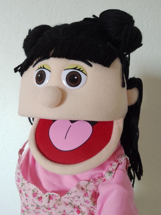 Gezicht van een handpop met open mond, bruine ogen, en zwart haar in knotjes. Draagt een roze jurkje.