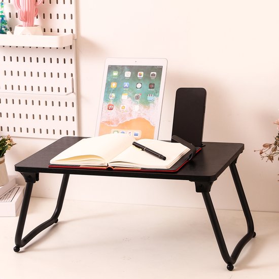 Zwart bedtafeltje met opgevouwen poten, met een tablet, boek, pen en telefoon.
