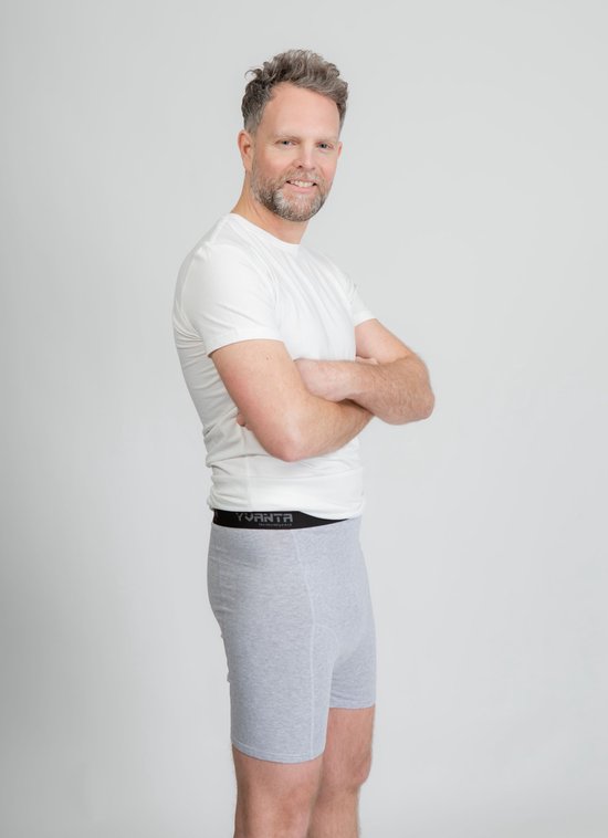Man met een grijze boxer met grijze elastische band met Yvanta-logo, met armen gekruist over zijn borst. Een witte t-shirt is opgestroopt.