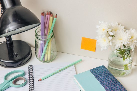 Bureau met een lamp, potloden in een pot, notitieboekjes, schaar en bloemen.