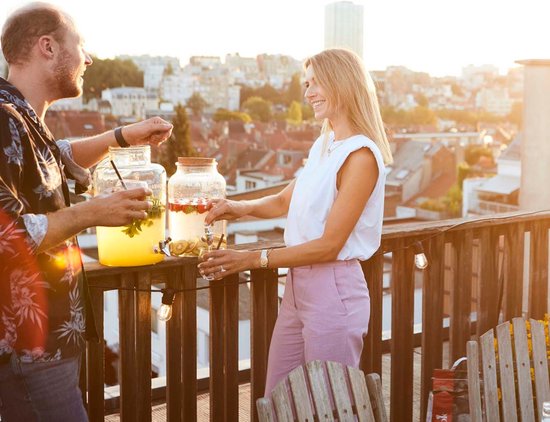 Man en vrouw op een balkon bij zonsondergang, met drankdispensers gevuld met zomerse dranken.